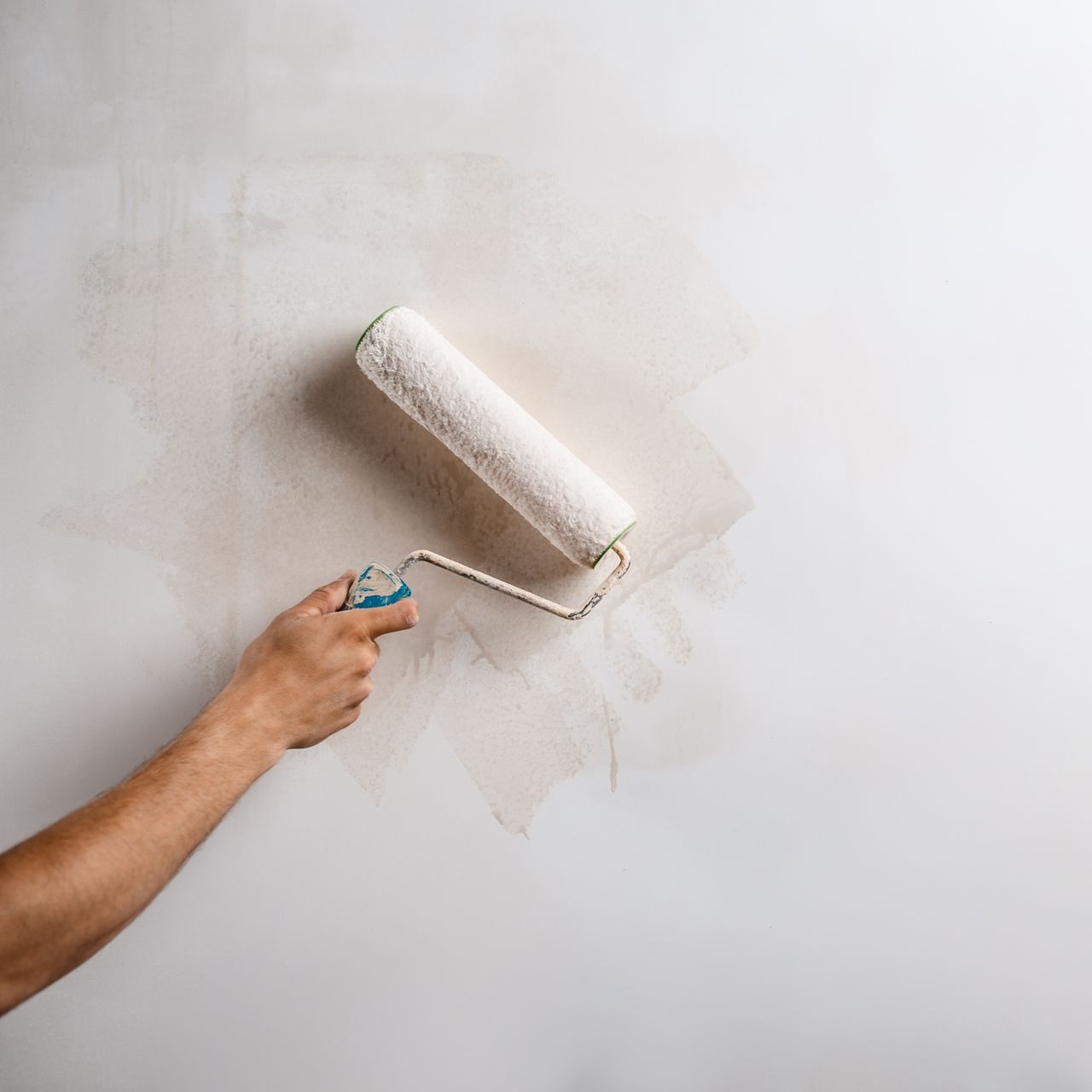 Main utilisant un rouleau à peinture pour appliquer de la peinture sur un mur.