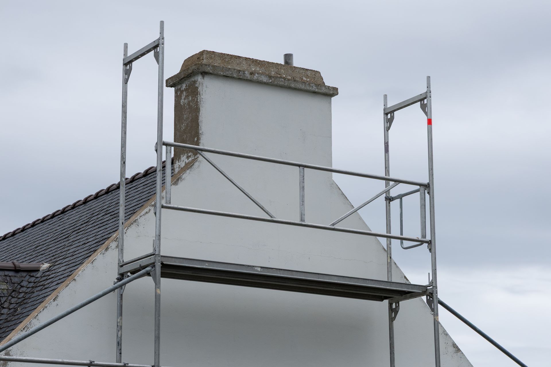 Échafaudage autour d'une cheminée blanche sur le toit d'une maison. Ciel gris en arrière-plan.