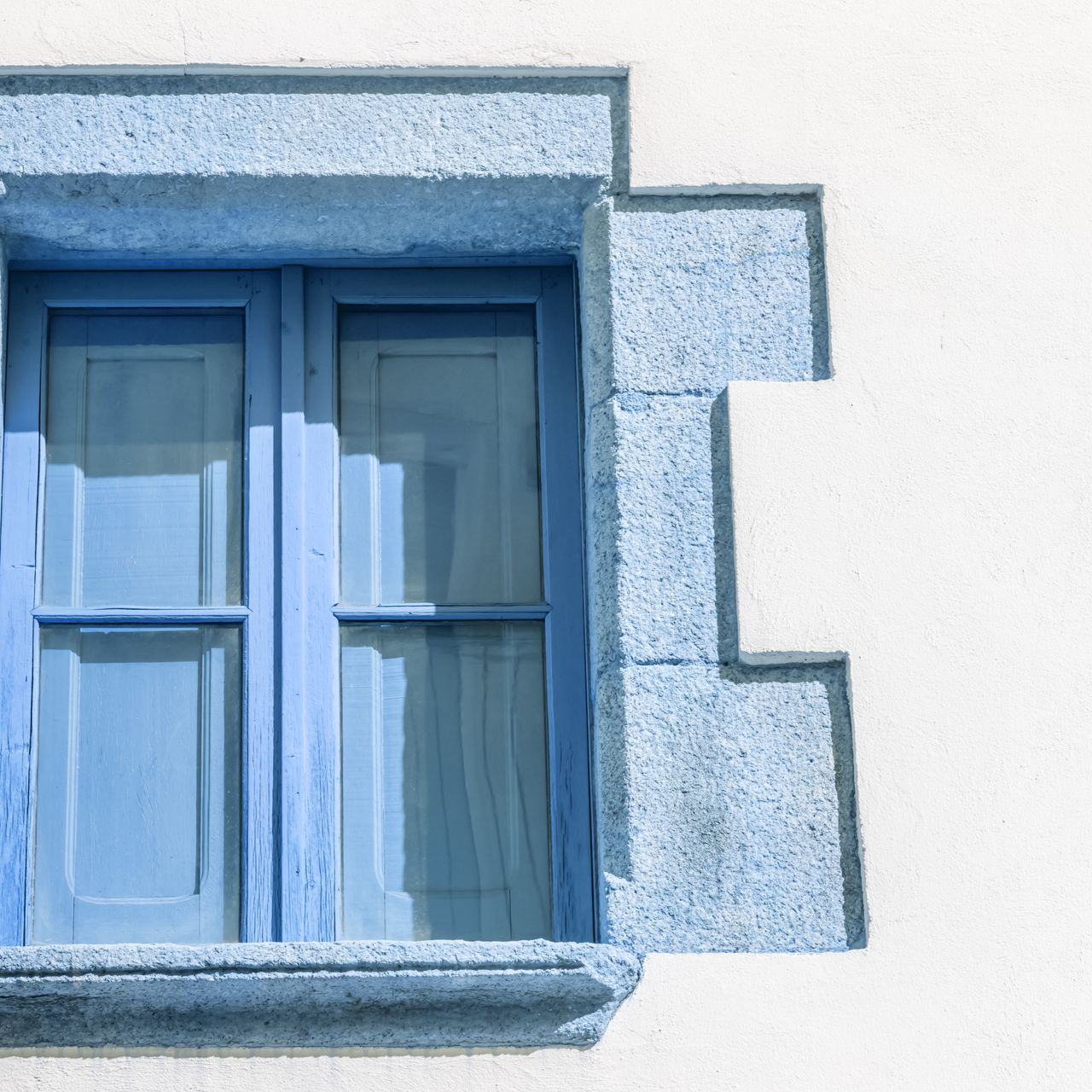 Fenêtre bleue avec garniture en pierre ornée sur un mur blanc.