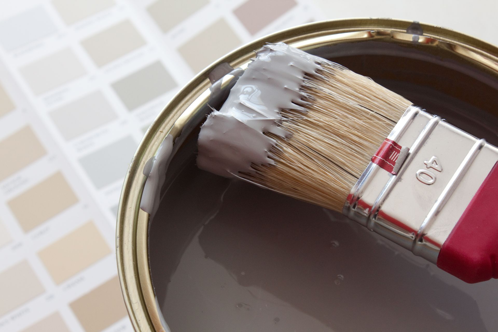 Pinceau dans un pot de peinture grise, avec des échantillons de couleur en arrière-plan.