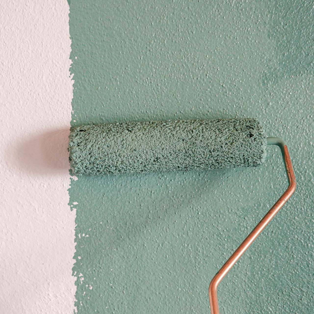 Rouleau à peinture appliquant de la peinture bleu sarcelle sur un mur blanc.