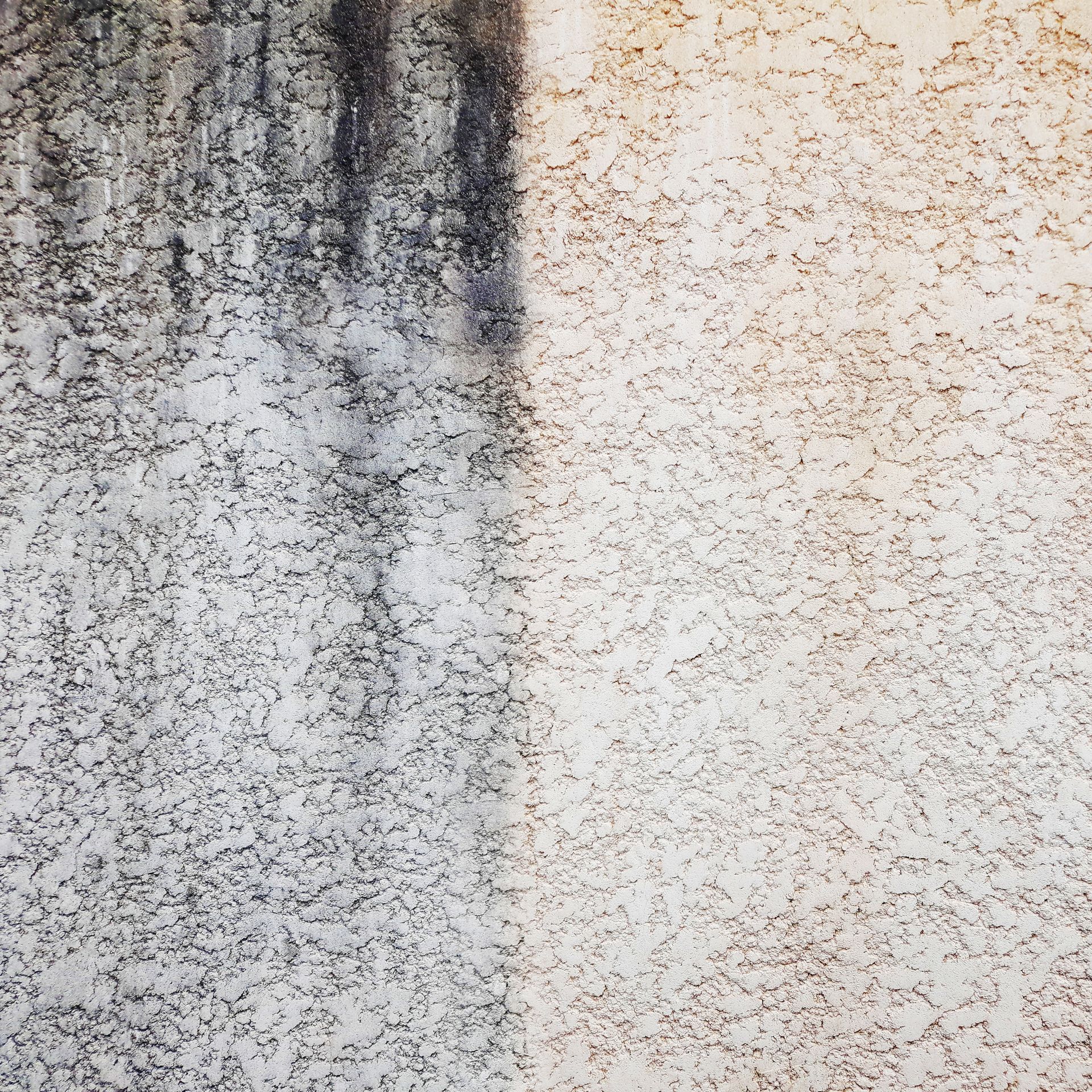 Mur en stuc à moitié nettoyé. Côté gauche : sombre et taché. Côté droit : clair et propre.