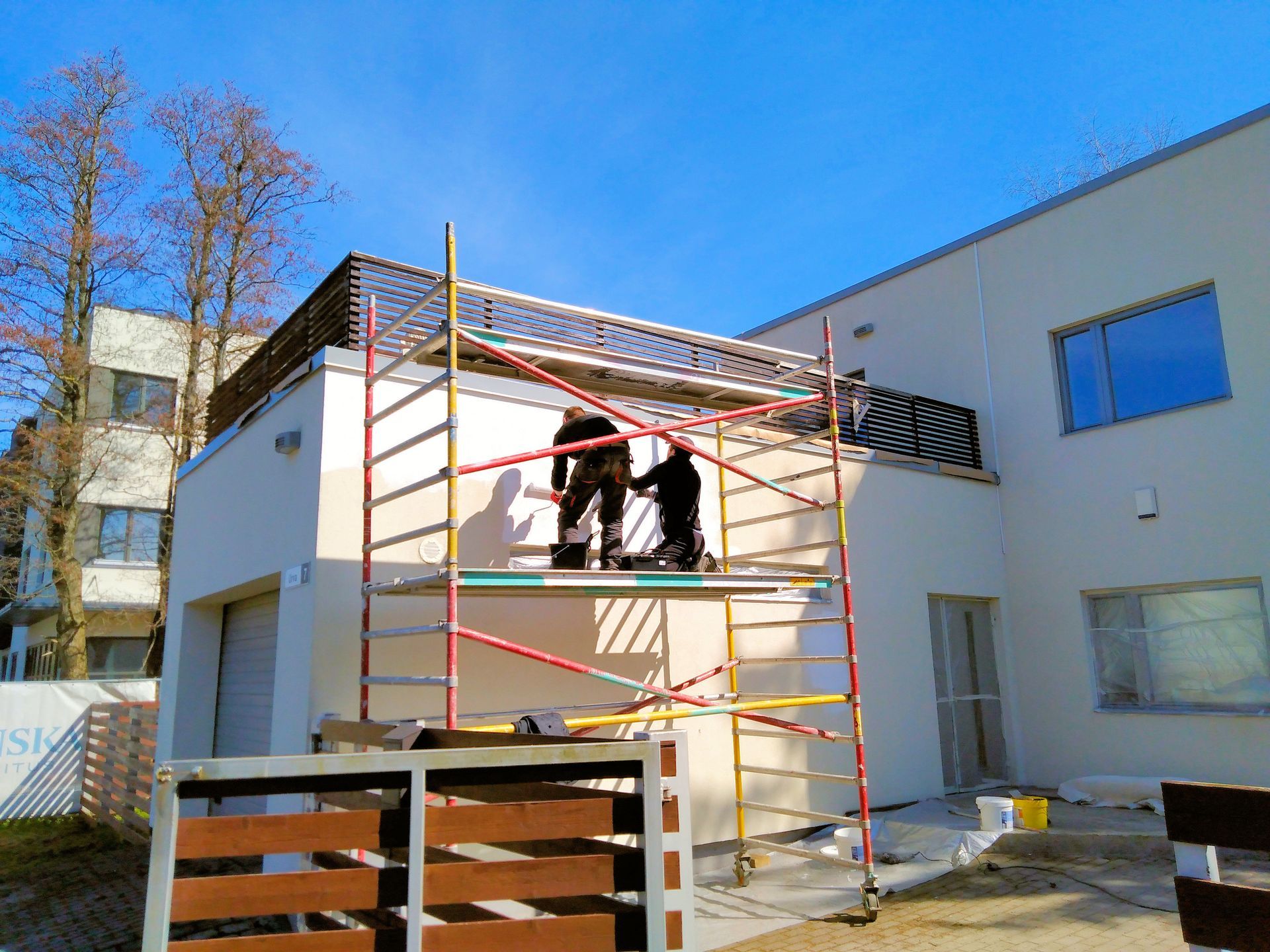 Deux ouvriers sur un échafaudage peignent l'extérieur d'un bâtiment blanc par une journée ensoleillée.