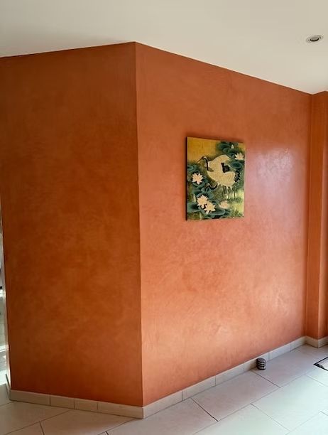 Coin de pièce peint en orange avec un tableau. Le mur présente un effet texturé ; le sol est carrelé blanc.