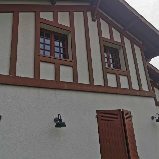 Façade d'un bâtiment à colombages en stuc blanc et à encadrements rouges, avec de petites fenêtres et une porte