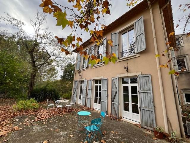 Maison beige aux portes et fenêtres ouvertes, chaises turquoise et feuilles d'automne dans une cour-jardin