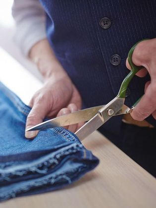 Una persona está cortando un par de jeans con tijeras.
