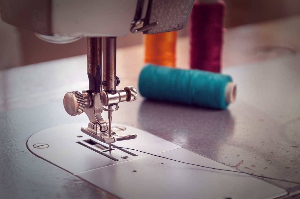 Un primer plano de una máquina de coser con carretes de hilo en el fondo.