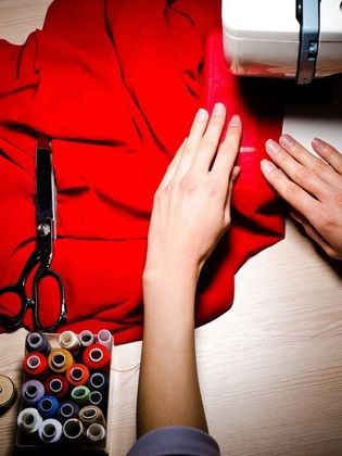 Una mujer está usando una máquina de coser para cortar un trozo de tela roja.