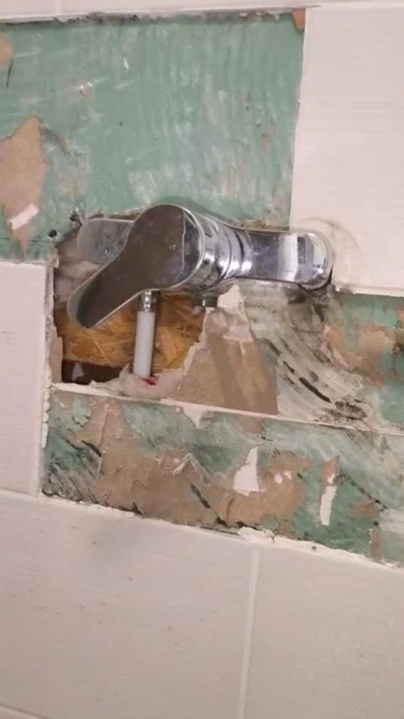 Robinet de douche installé dans un mur. Le mur est endommagé et carrelé.