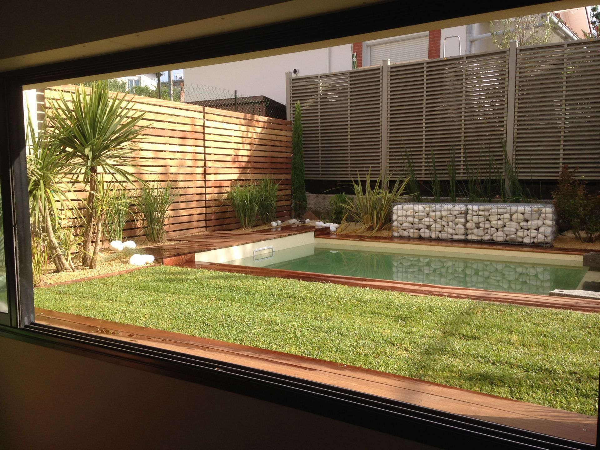 Photo du jardin d'une maison avec de l'herbe en premier plan et une piscine creusée en second plan.