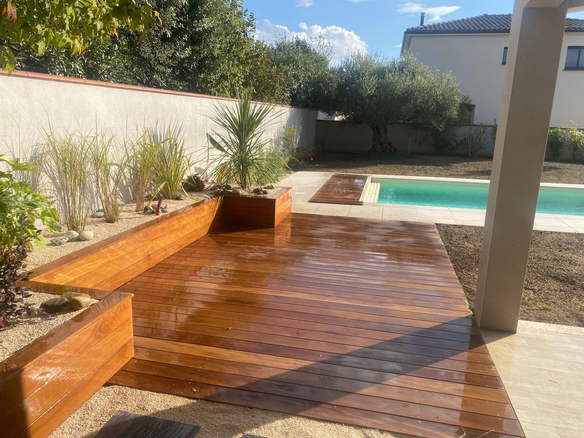 Terrasse en bois avec jardinières et espace piscine dans un jardin ensoleillé.
