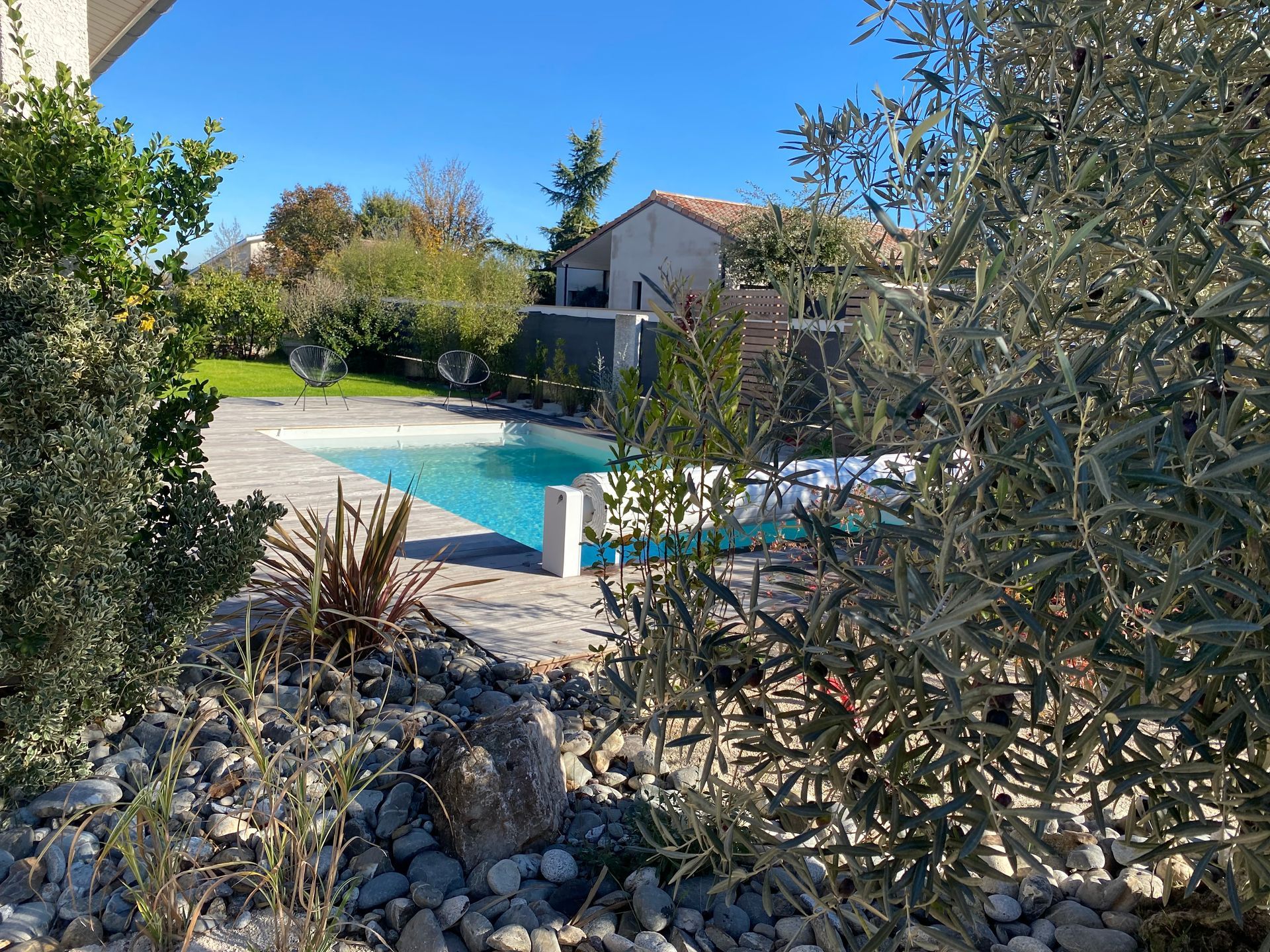 Piscine aux eaux turquoise entourée de jardins, d'arbres et d'une maison.