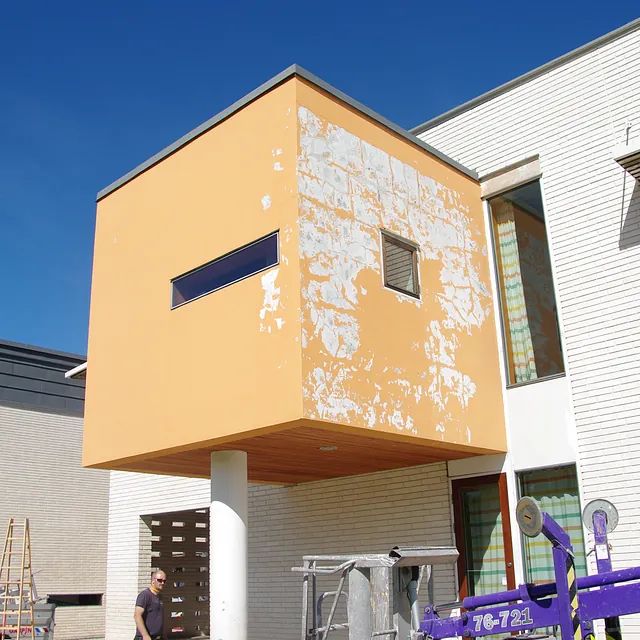 Ein Mann steht vor einem Gebäude mit einem lilafarbenen Aufzug, auf dem 76-720 steht