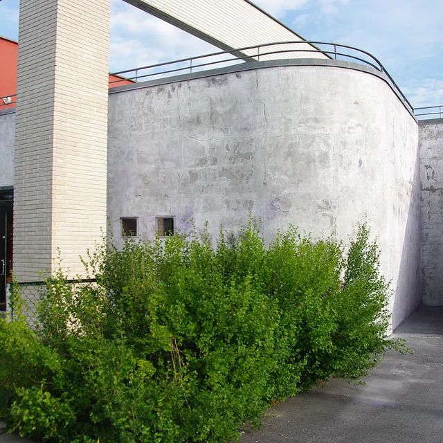 Ein weißes Gebäude mit einer Ziegelsäule und ein paar Büschen davor