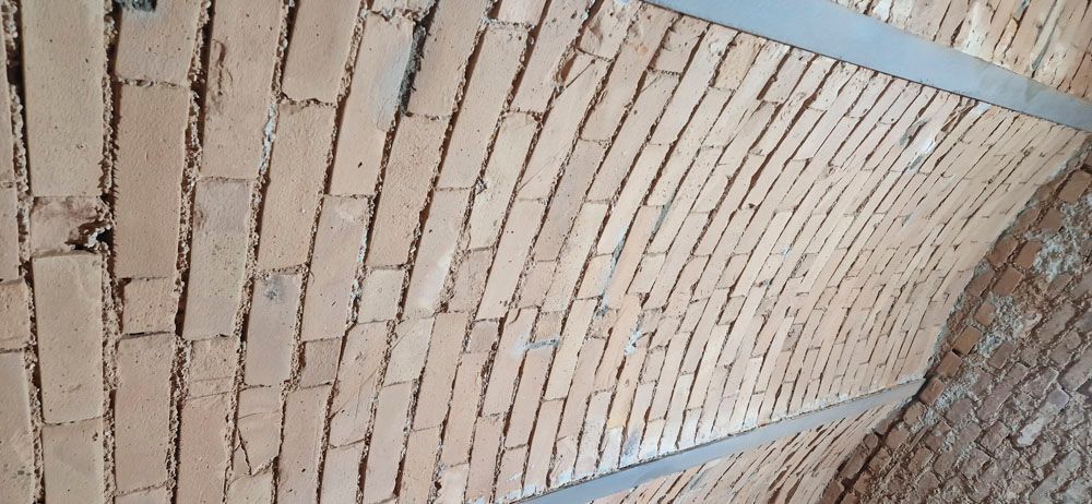 Gewölbte Ziegeldecke mit Mörtelfugen. Zwei Metallträger verlaufen oben quer.