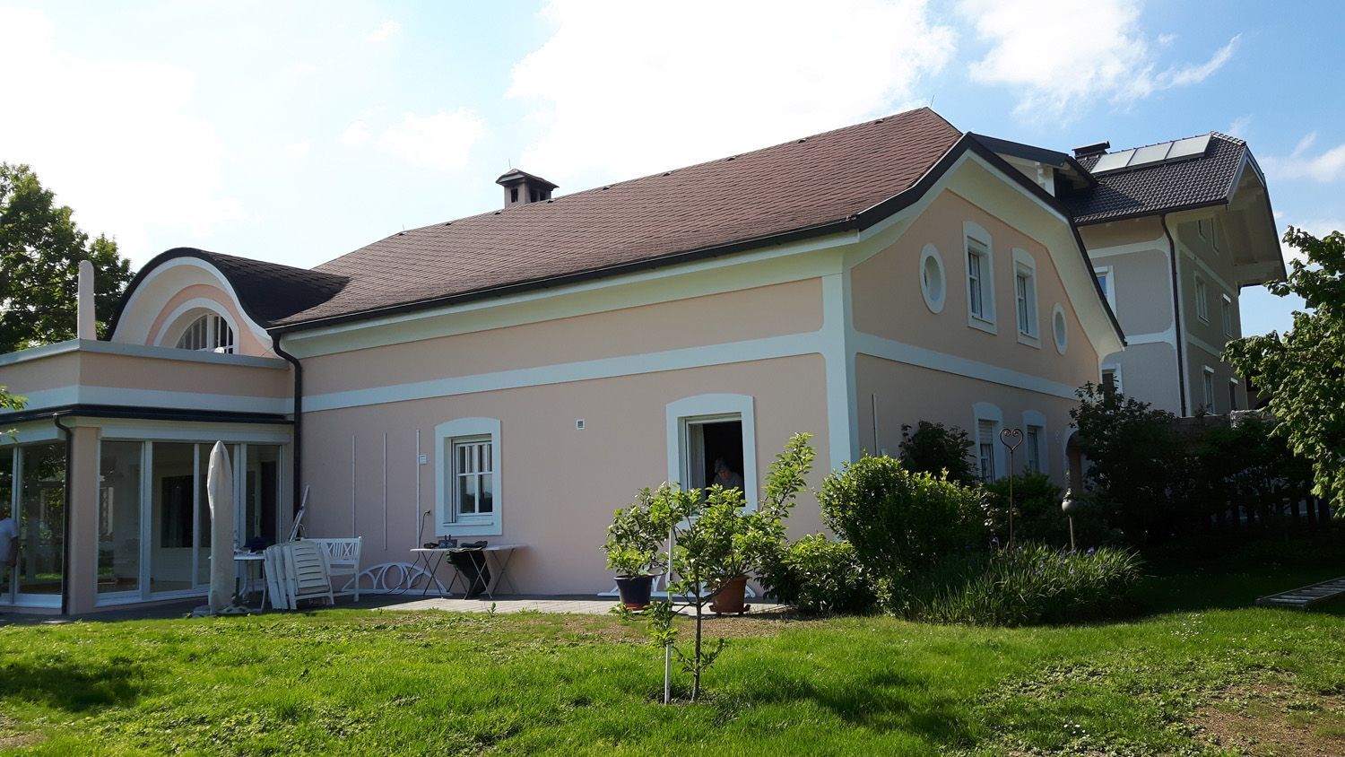 Ein großes rosa Haus mit einem roten Ziegeldach steht inmitten einer üppigen grünen Wiese.