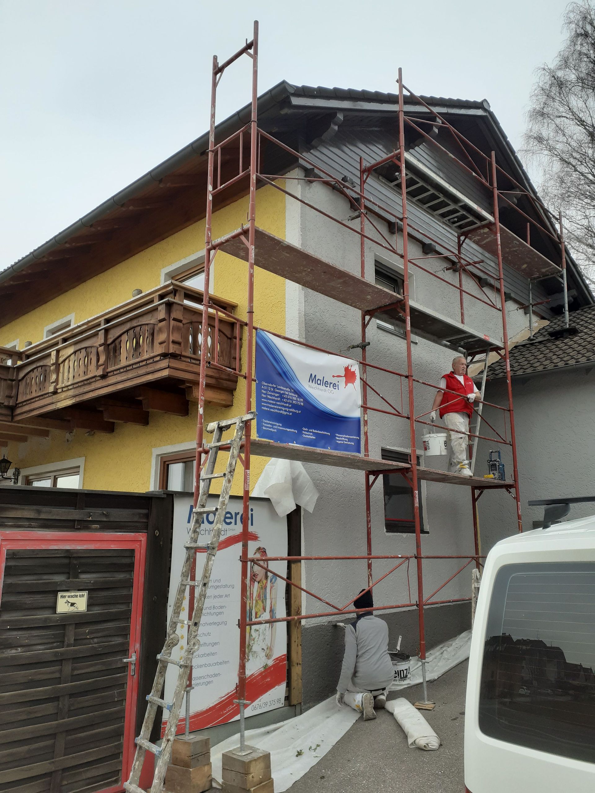 Ein Mann streicht die Seite eines Hauses mit Gerüst.