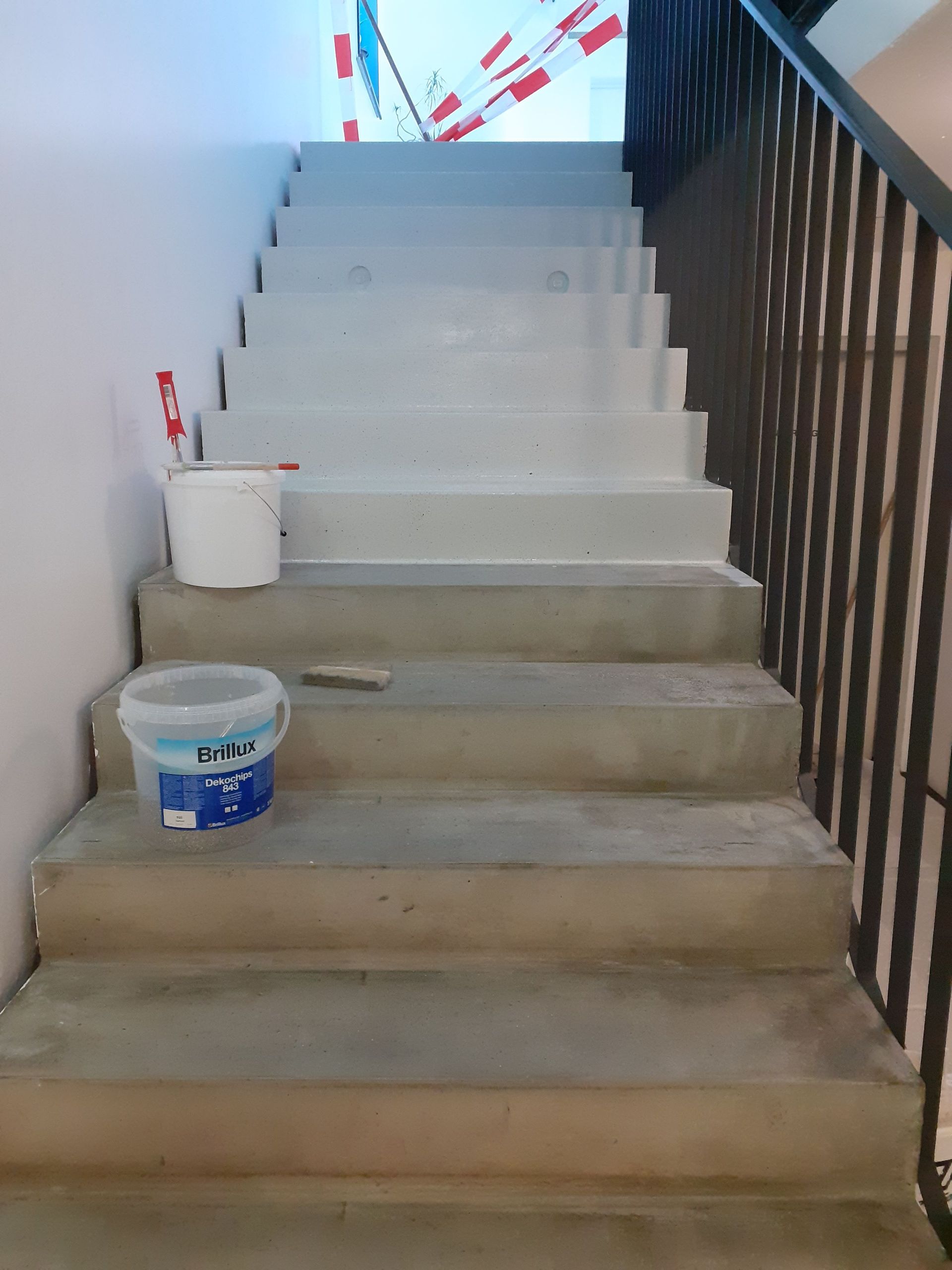 Auf den Stufen einer Treppe steht ein Eimer Farbe.