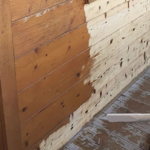 Eine Person streicht eine Holzwand mit weißer Farbe.