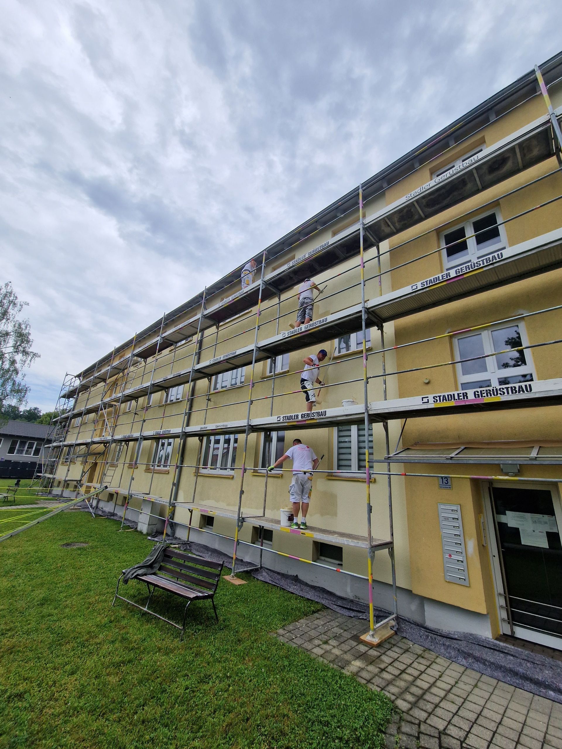 Ein Mann streicht die Seite eines Gebäudes mit Gerüst.