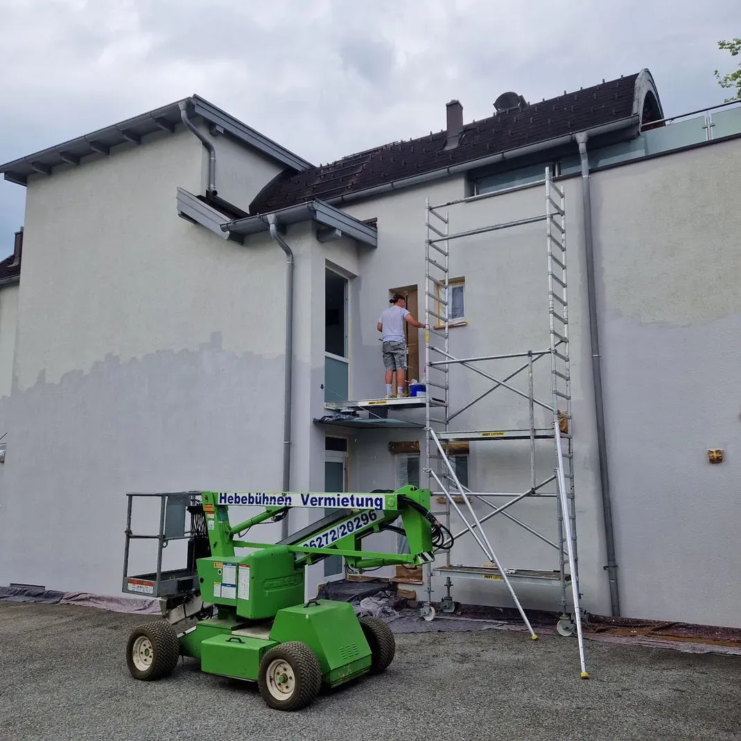 Ein Mann streicht die Seite eines Gebäudes mit einem grünen Aufzug.