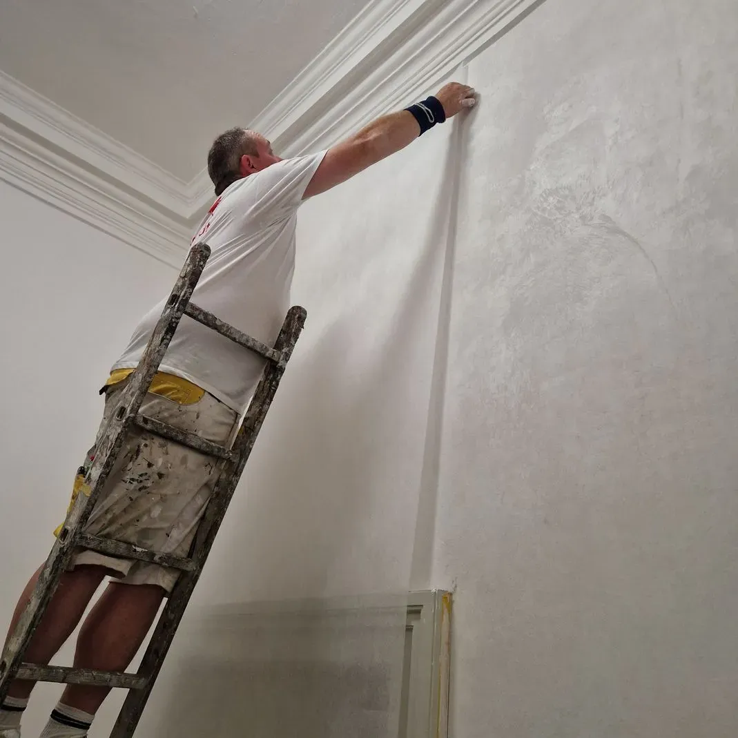 Ein Mann steht auf einer Leiter und streicht eine Wand