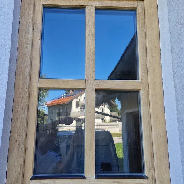 Ein Holzfenster mit der Spiegelung eines Hauses darin