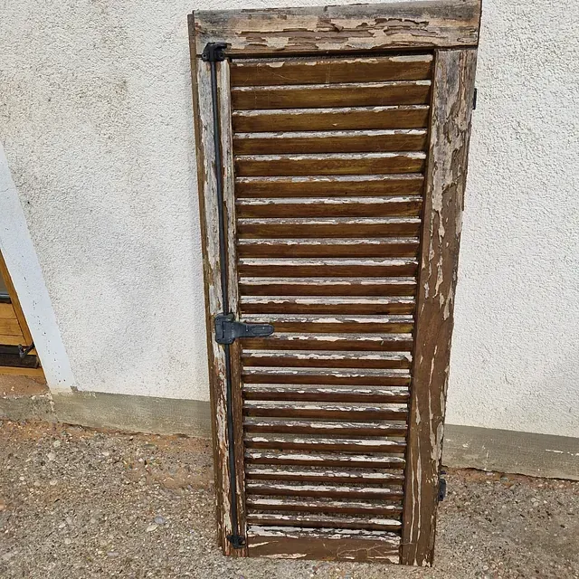 Ein Holzfensterladen liegt auf dem Boden vor einer weißen Wand