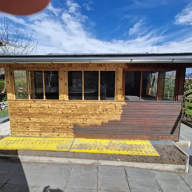 Ein Holzhaus mit vielen Fenstern wird gestrichen