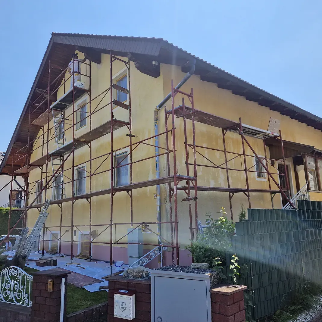 Ein gelbes Haus mit einem Gerüst darum wird gestrichen.