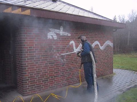 Ein Mann reinigt eine Ziegelwand mit einem Hochdruckreiniger.