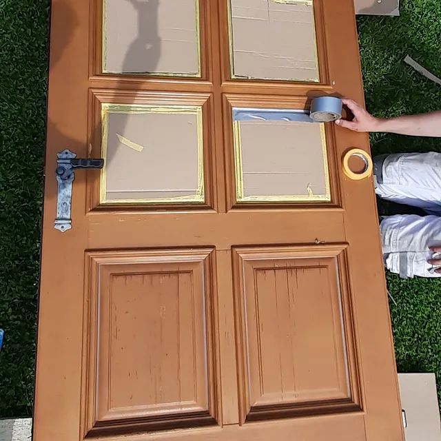 Eine Person klebt eine Holztür mit Klebeband zu.