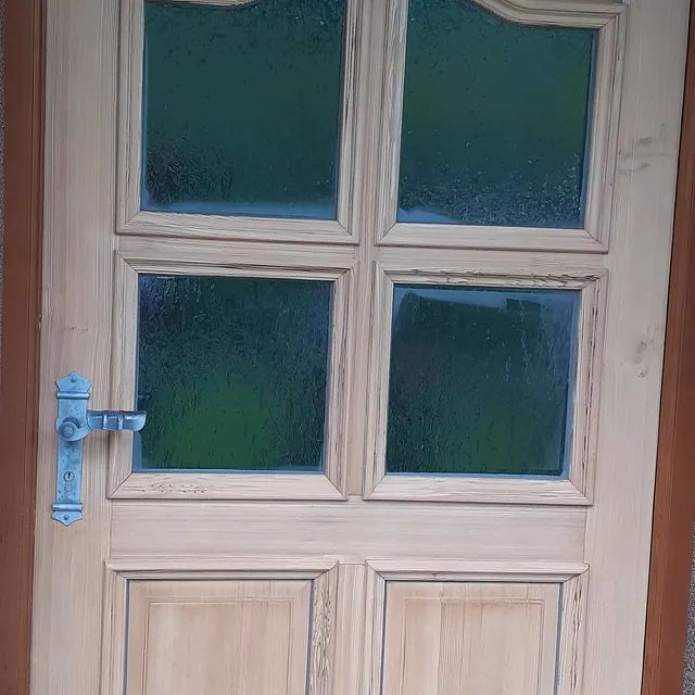 Eine Holztür mit vier Fenstern und einer blauen Klinke.