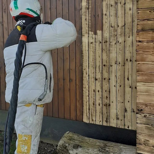 Eine Person steht vor einer Holzwand und hält einen Regenschirm.