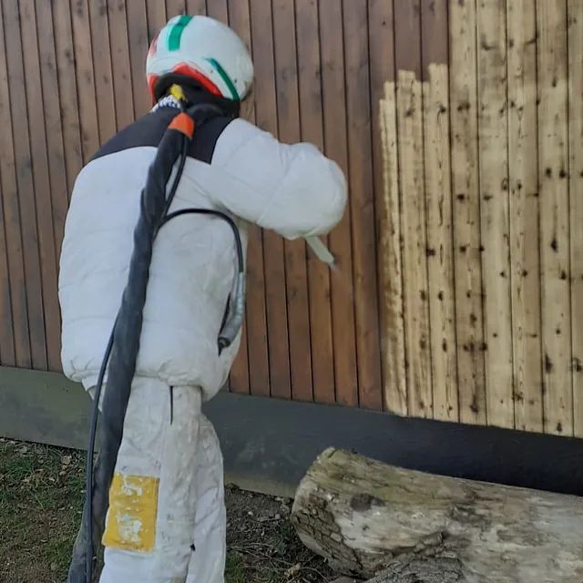 Ein Mann mit Helm sandstrahlt eine Holzwand