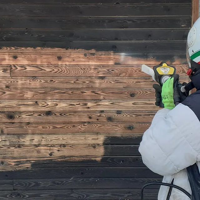 Eine Person mit Helm und Handschuhen steht vor einer Holzwand.