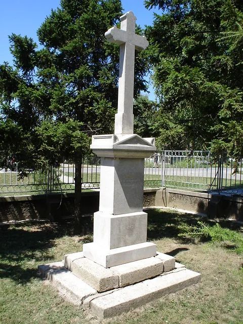 Eine Statue eines Kreuzes auf einem Friedhof mit Bäumen im Hintergrund