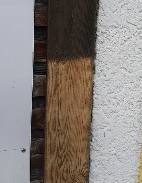 Neben einer weißen Wand liegt ein Stück Holz.