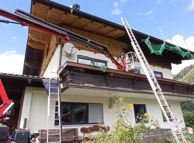 Ein Kran hebt eine Leiter auf das Dach eines Hauses.