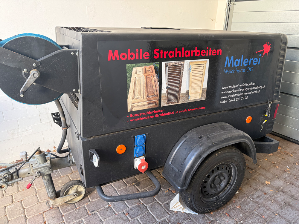 Schwarze mobile Sandstrahlanlage auf einem Anhänger mit Logo.