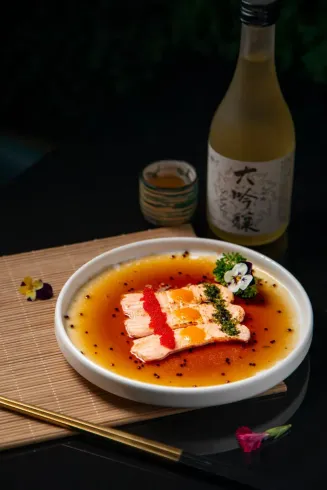Un plato de sashimi de salmón sellado en salsa ponzu con huevas, junto a una botella de sake y una taza