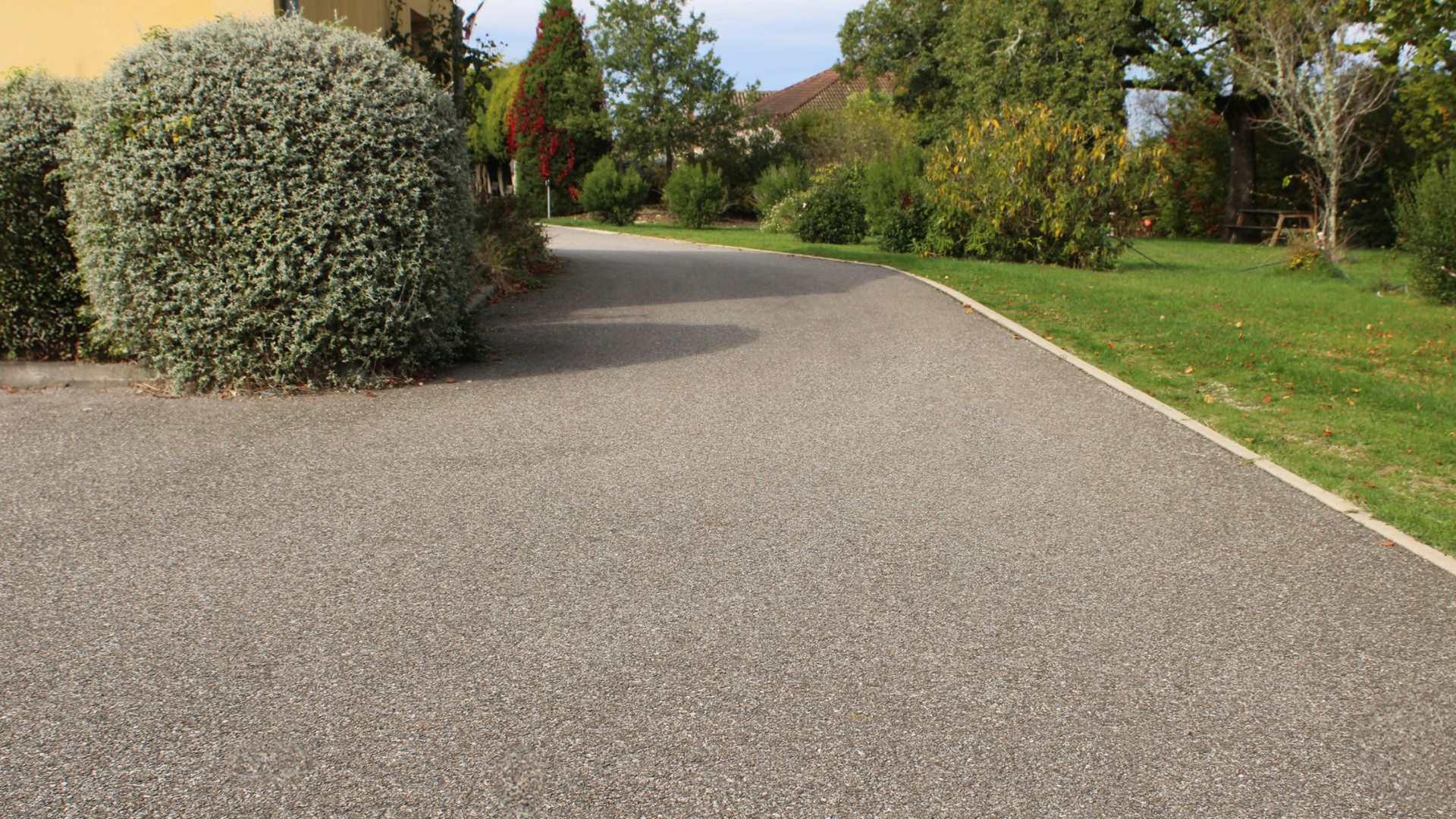 Allée de gravier bordée de verdure soignée de part et d'autre, menant à une maison éloignée.