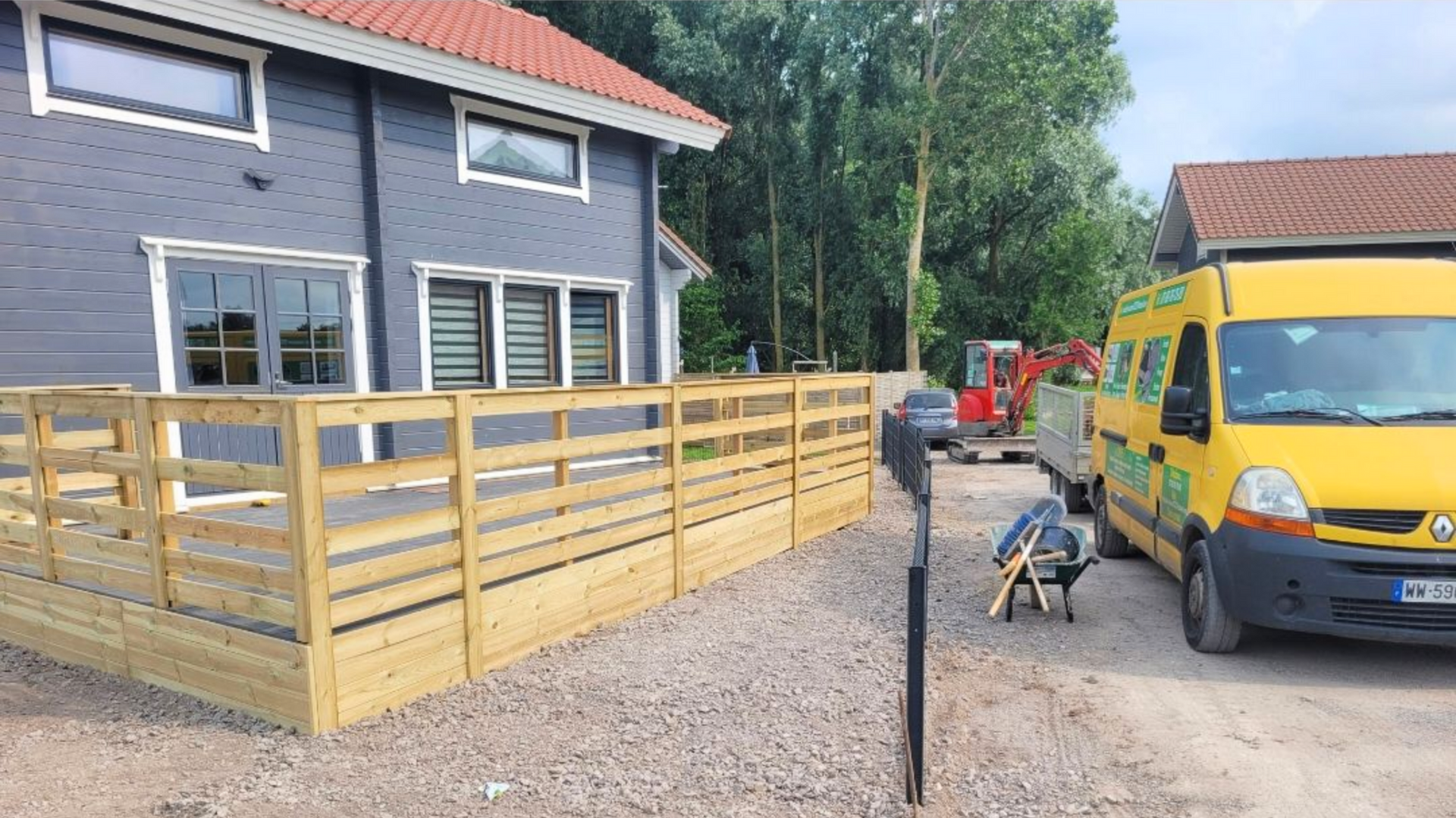 Une maison grise avec une clôture en bois et une camionnette de chantier jaune garée devant.