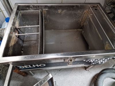 Panier à friture en acier inoxydable ouvert dans une friteuse professionnelle, partiellement rempli d’huile et de graisse.