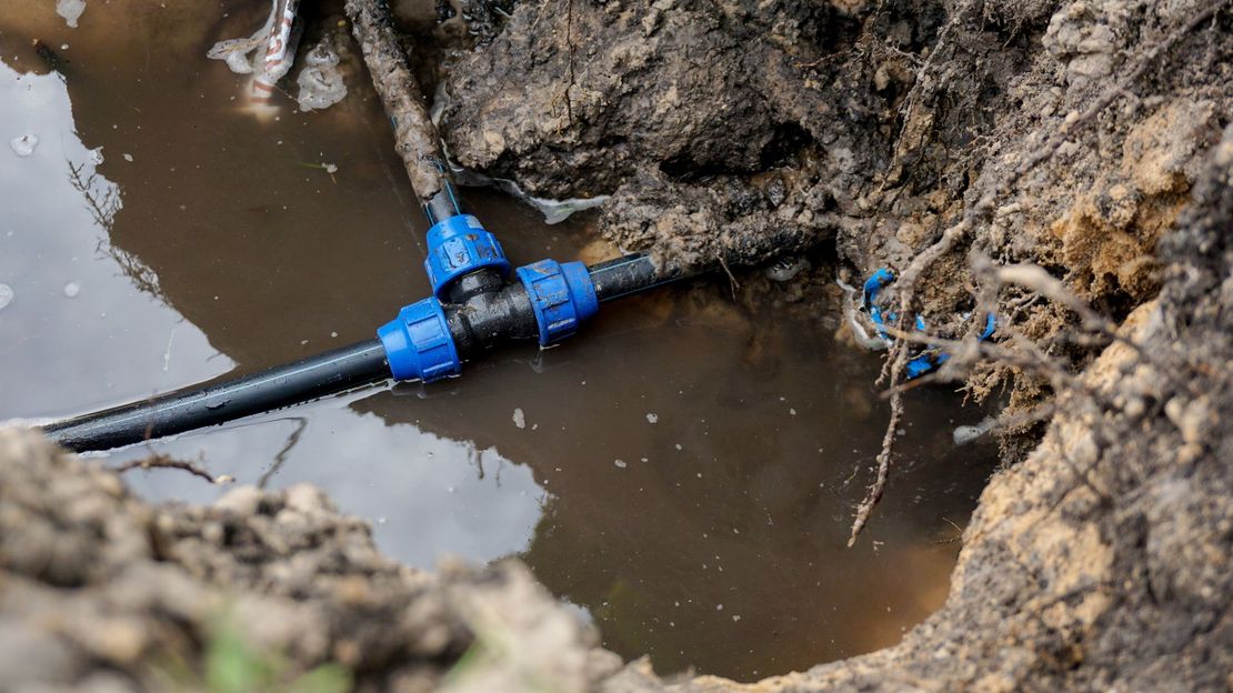Raccord de tuyau dans une tranchée boueuse, avec de l’eau qui fuit autour de canalisations souterraines à découvert.
