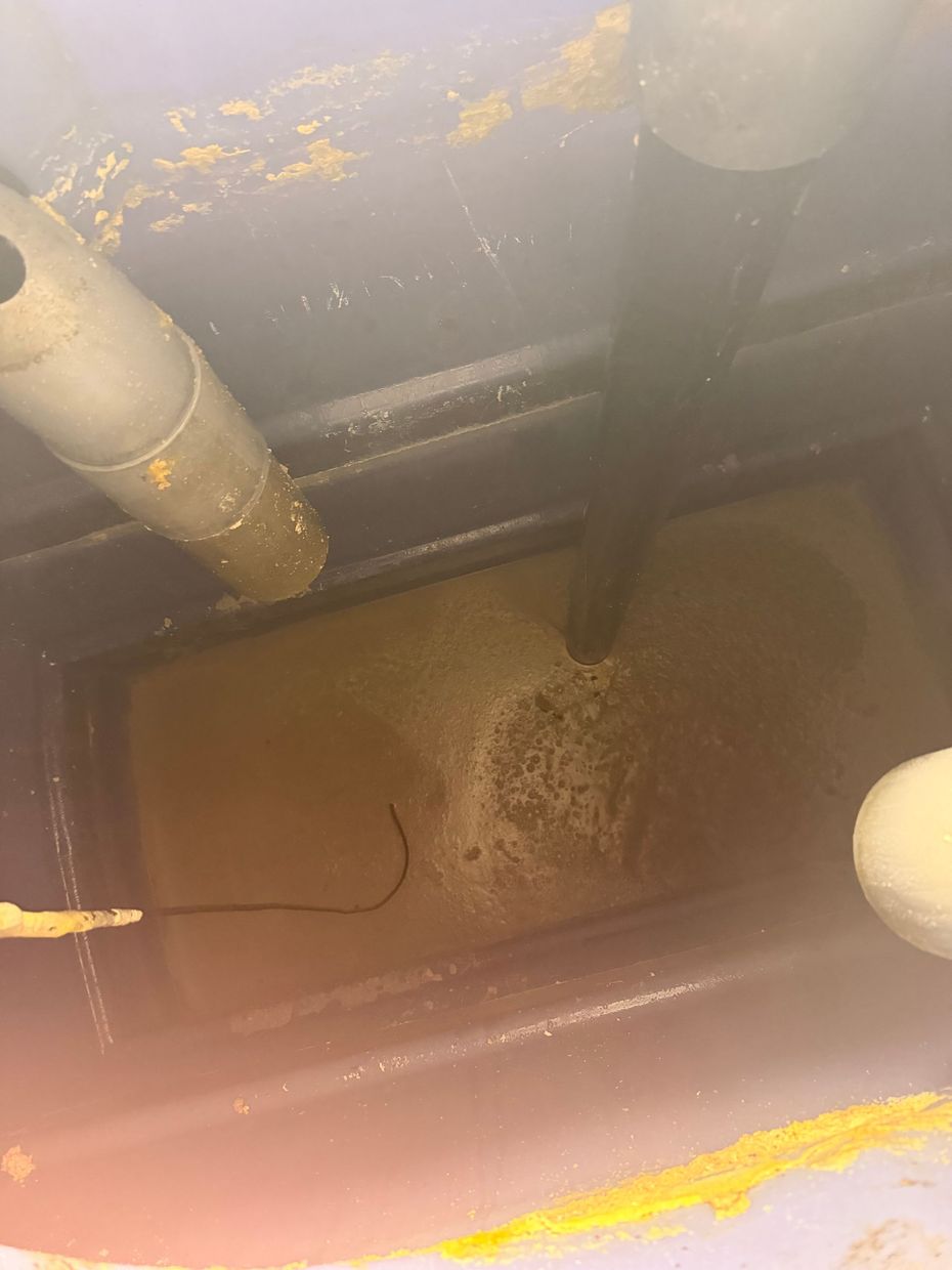 Intérieur d’une cuve ou d’un puisard sale, avec des tuyaux, une eau trouble et une accumulation de sédiments.