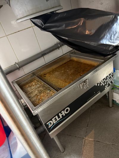 Friteuse ouverte avec de l’huile et des résidus alimentaires dans une cuisine carrelée.