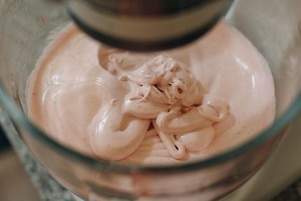 Batidora de mano batiendo una masa rosa pálida en un recipiente de vidrio.