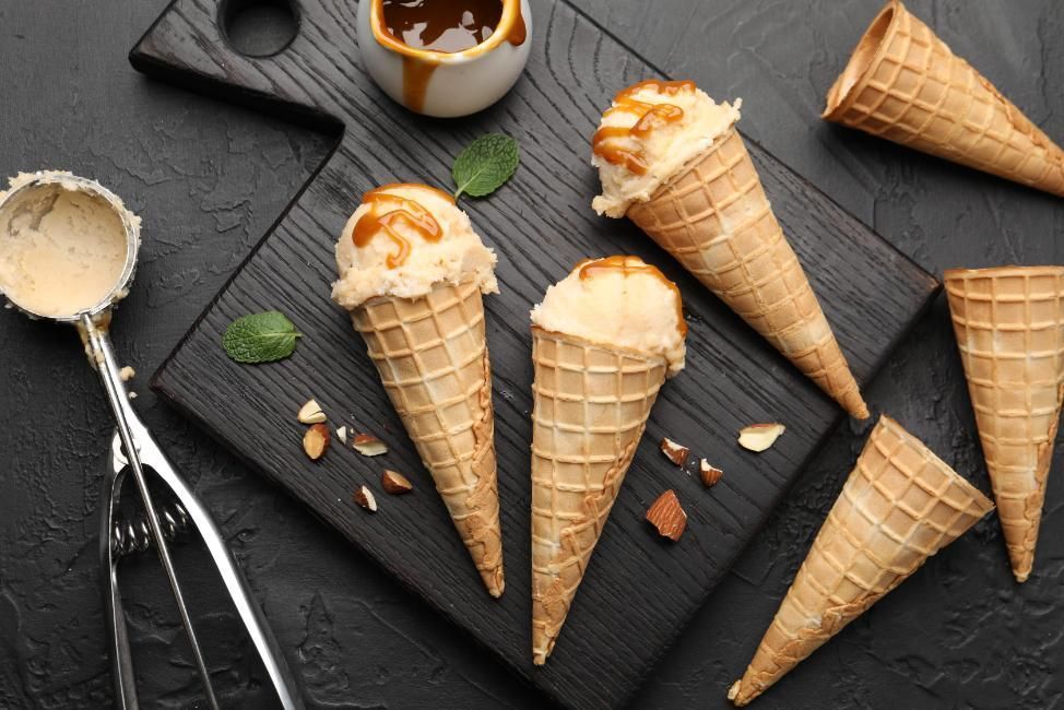 Conos de helado con bolas sobre una superficie de pizarra oscura, con salsa de caramelo y hojas de menta.